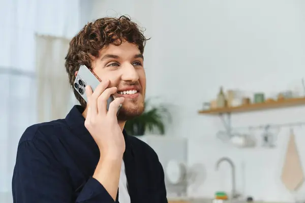 Homme aux cheveux bouclés profite d'une conversation animée sur son smartphone dans un appartement élégant. — Photo de stock