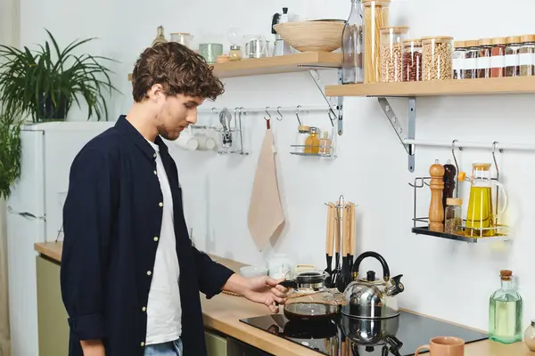 A handsome young man prepares coffee in his elegant kitchen, enjoying the cozy atmosphere. — Stock Photo