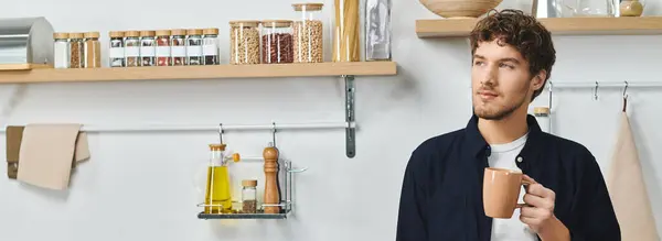 Um jovem bonito toma café em sua cozinha aconchegante, banner — Fotografia de Stock