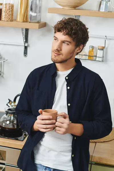 Handsome young man in a shirt holds a cup while contemplating in his inviting apartment. — Stock Photo