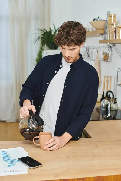 Curly-haired man stands at a kitchen counter pouring coffee into a mug in his stylish home. — Stock Photo