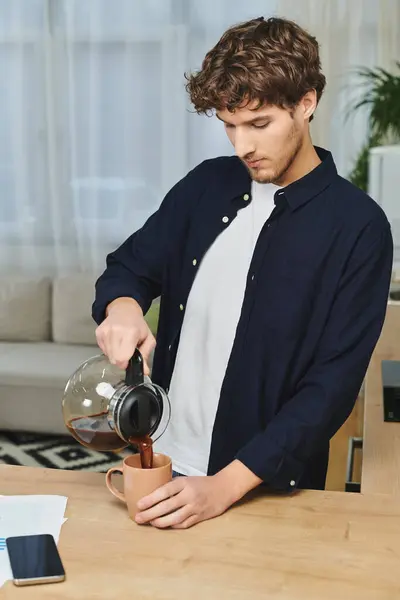 Joven con el pelo rizado vierte café en una taza en su apartamento moderno, abrazando la tranquilidad. - foto de stock