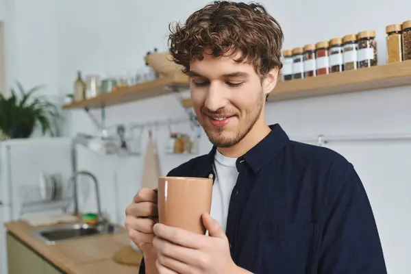 Красивий молодий чоловік з кучерявим волоссям рятує гарячий напій у своєму сучасному будинку. — стокове фото