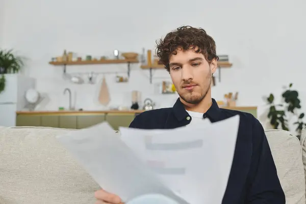 Curly haired man is focused on reading documents while relaxing in a contemporary living space. — Stock Photo