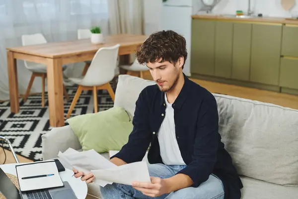 Curly-haired man sits on a couch, examining important papers in a modern living space. — Stock Photo