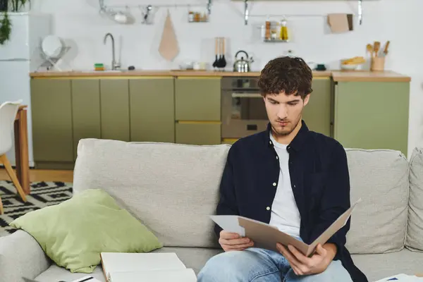 Curly-haired young man sits comfortably on a couch, examining papers in his chic living space. — Stock Photo