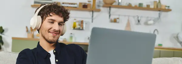 Curly-haired cara relaxa confortavelmente em casa, focado em seu laptop como ele ouve música, banner — Fotografia de Stock
