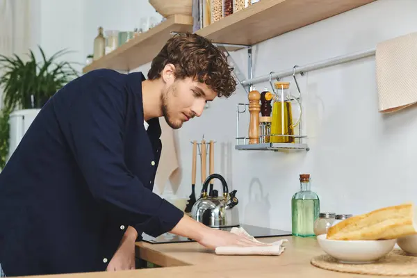 Jovem bonito em uma camisa casual limpa seu balcão de cozinha com cuidado em casa. — Fotografia de Stock
