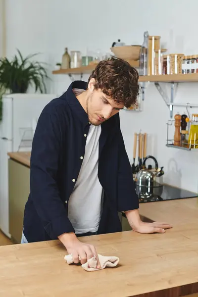 Bonito jovem com cabelo encaracolado está limpando sua bancada de cozinha elegante em casa — Fotografia de Stock
