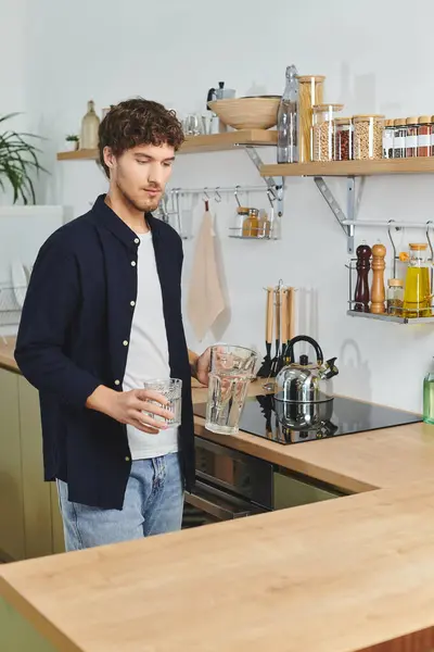 Jovem bonito com cabelo encaracolado derrama bebidas em sua elegante cozinha moderna, relaxando dentro de casa. — Fotografia de Stock