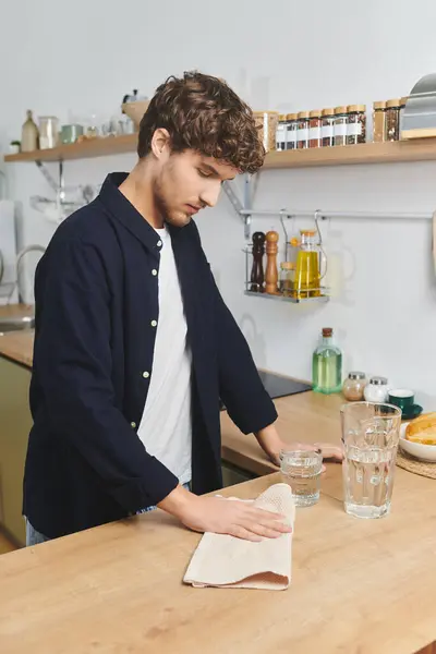 Jovem bonito com cabelo encaracolado limpa o balcão da cozinha enquanto desfruta de um momento tranquilo. — Fotografia de Stock