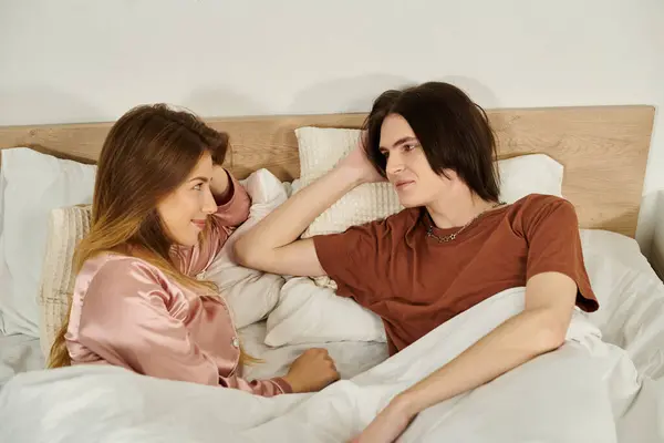 Young couple relaxes and smiles at each other in a cozy bedroom while lounging in bed. — Stock Photo