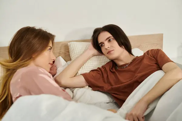 Una joven pareja se relaja en la cama, disfrutando de una conversación tranquila mientras está envuelta en suaves mantas. - foto de stock