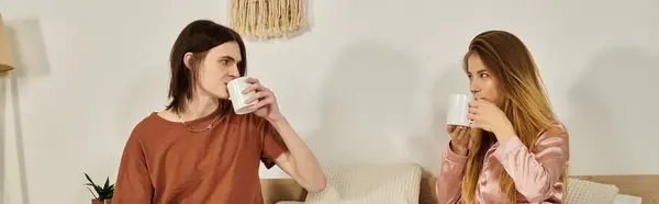 Two stylish young individuals share a cozy moment, sipping from mugs and smiling at each other. — Stock Photo