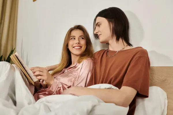 Due giovani adulti condividono un momento accogliente a letto, godendo di un libro mentre si scambiano sorrisi caldi. — Foto stock