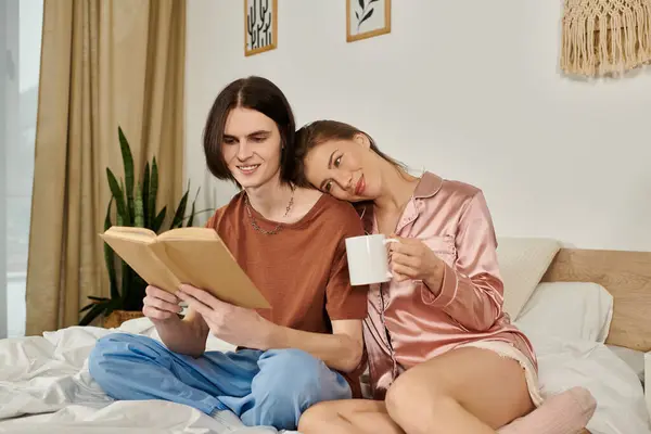 A chic young couple shares a relaxed morning, sipping coffee and enjoying a book in bed. — Stock Photo