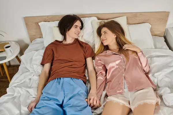 Un jeune couple se couche sur un lit, profitant d'un moment tendre tout en se tenant la main et en souriant. — Photo de stock