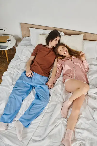 Una joven pareja sonríe cálidamente, relajados juntos en una cama durante una tarde perezosa. - foto de stock