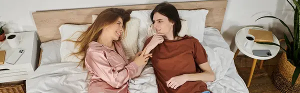 Una joven pareja yace junta en una cama, riendo y disfrutando de una interacción lúdica en una acogedora habitación. - foto de stock