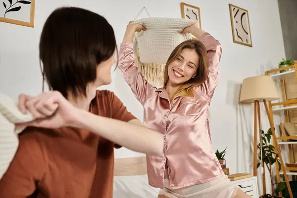 A young duo shares laughter and joy while playfully tossing pillows together in a chic living space. — Stock Photo