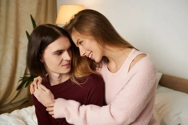 Two young adults enjoy a loving embrace, smiling warmly at each other in a softly lit bedroom. — Stock Photo