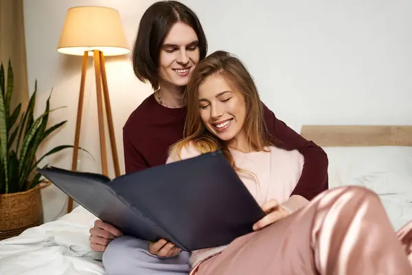A young couple smiles joyfully while sharing a book in their cozy bedroom filled with warmth. — Stock Photo