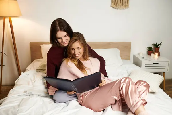 A stylish young couple sits on a bed, happily sharing smiles while browsing a photo album. — Stock Photo