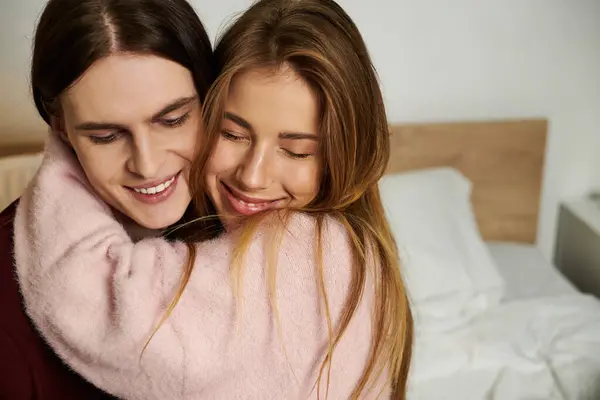 Una giovane coppia condivide un caldo abbraccio, sorridendo gioiosamente in una camera da letto elegante piena di luce. — Foto stock