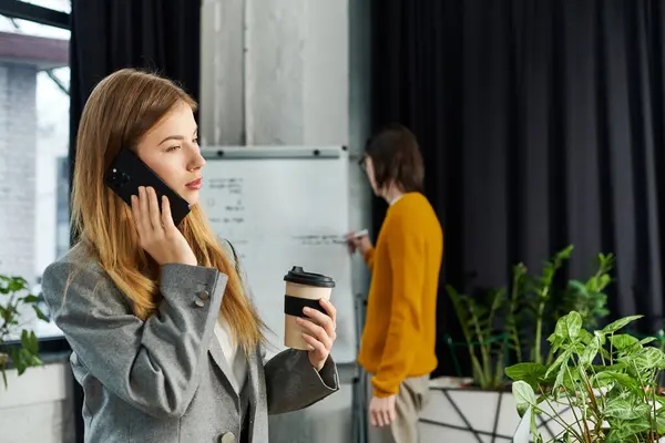 Une jeune personne profite d'une conversation téléphonique à côté de sa collègue dans un espace de travail moderne. — Photo de stock