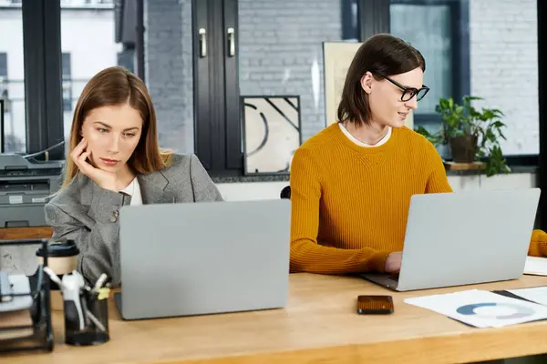 Deux jeunes personnes élégantes se concentrent sur leurs ordinateurs portables dans un espace de travail lumineux et contemporain. — Photo de stock