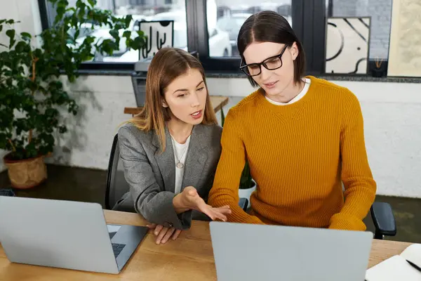 Two young individuals engage in a lively discussion while working on laptops in a stylish workspace. — Stock Photo