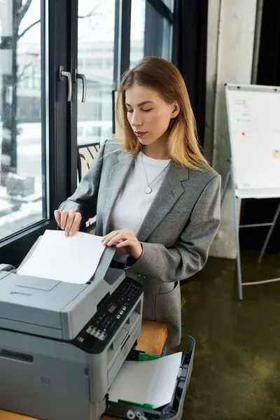 Stylish young woman uses a printer in an office with big windows and snowy scenery outside. — Stock Photo