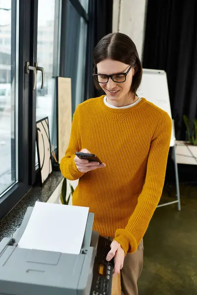 A young individual wearing a stylish sweater checks their smartphone as they stand by a printer. — Stock Photo