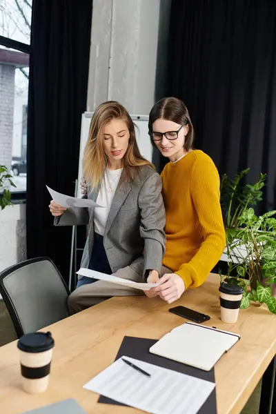 Deux jeunes en tenue élégante discutent de papiers tout en étant entourés de verdure et de tasses à café. — Photo de stock