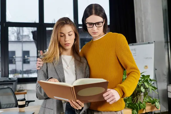 Two stylish individuals engage with a book, sharing insights in an inspiring modern office setting. — Stock Photo