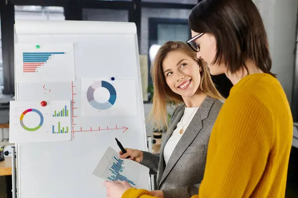 Dois jovens conversam animadamente sobre gráficos coloridos em um espaço de trabalho brilhante. — Fotografia de Stock