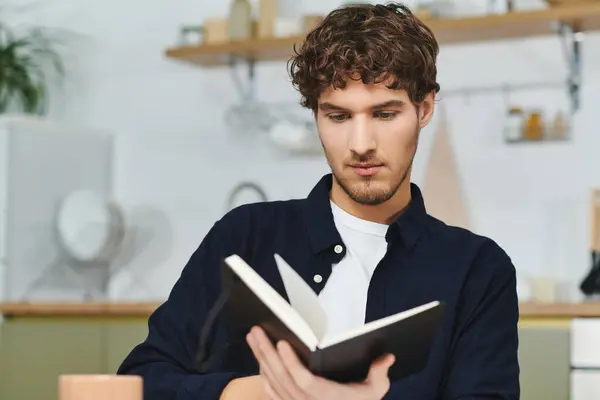 Handsome young man with curly hair enjoys reading in his stylish, contemporary home setting. — Stock Photo