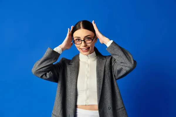 Junge Frau in stylischem Outfit strahlt vor Aufregung, während sie vor blauem Hintergrund posiert. — Stockfoto