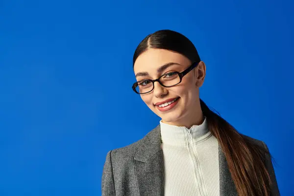 Una joven mujer se levanta alegremente con confianza sobre un fondo azul brillante. - foto de stock