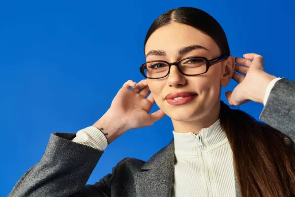 A young, beautiful woman with glasses playfully adjusts her hair, exuding confidence and joy. — Stock Photo