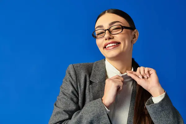 A joyful young woman in glasses playfully adjusts her collar while smiling brightly. — Stock Photo
