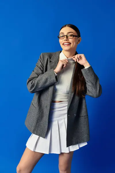 Radiating confidence, a young woman adjusts her collar while smiling amidst a vibrant blue backdrop. — Stock Photo