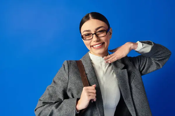 Mujer joven emocional en gafas elegantes y chaqueta gris expresa alegría y confianza al posar. - foto de stock