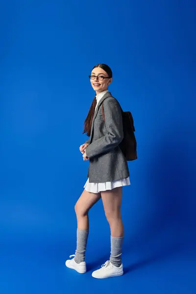 Uma jovem mulher com óculos mostra sua roupa elegante e atitude alegre em um cenário azul. — Fotografia de Stock