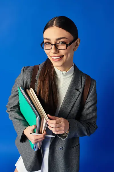 A cheerful young woman with glasses holds colorful books against a bright blue background. — Stock Photo