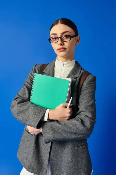 A young woman in stylish attire gazes confidently while holding a notebook and pen. — Stock Photo