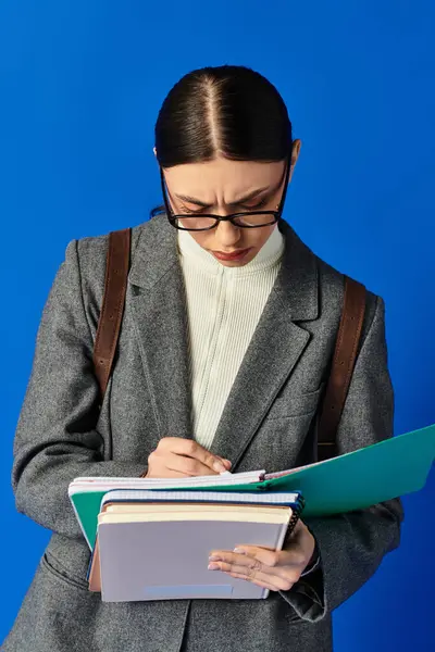 Une jeune femme en tenue formelle étudie ses notes tout en écrivant prudemment, perdue dans sa tâche. — Photo de stock