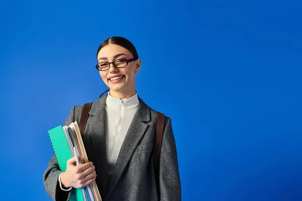 Confident young woman with glasses holds folders and smiles brightly in a vibrant setting. — Stock Photo