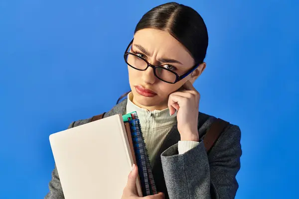 A young woman with glasses looks pensively to the side while holding a notebook, lost in thought. — Stock Photo