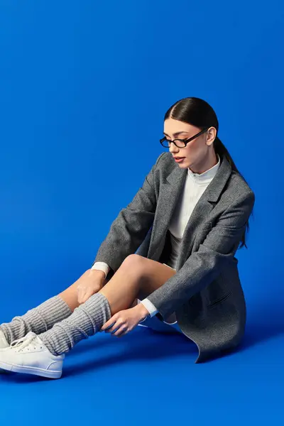 A beautiful young woman adjusts her cozy socks while sitting on a vibrant blue background. — Stock Photo